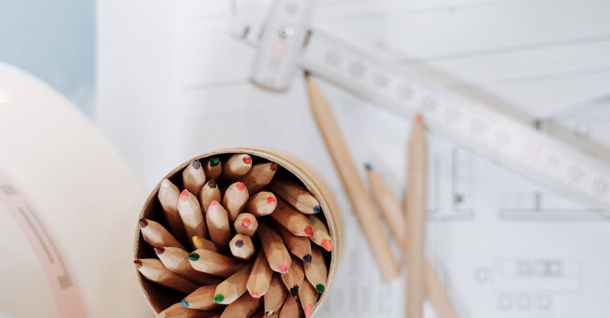 Overhead shot of a creative workspace featuring colored pencils, drafting plans, and measuring tools on a desk.